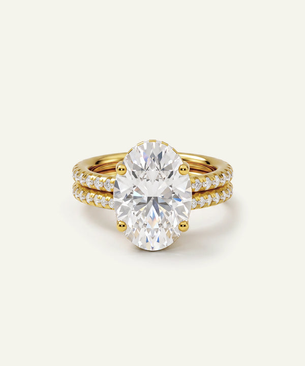 A yellow gold engagement ring featuring a large oval-cut clear center stone, with a matching gold wedding band set with small pavé diamonds, shown on a light cream background.
