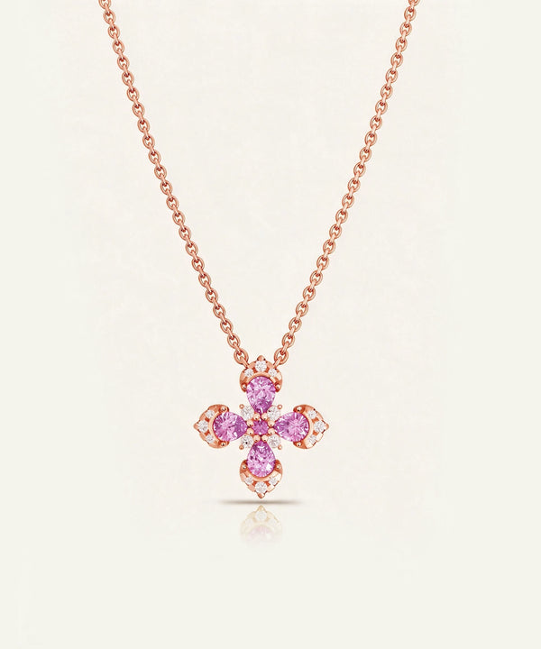 A rose gold necklace with a four-petal cross pendant featuring pink gemstones and small clear accent stones, displayed on a light cream background.