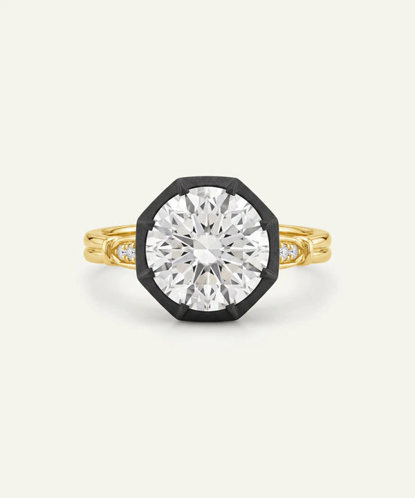A yellow gold octagonal ring with a large clear round-cut center stone and small side stones, set in a black bezel-like frame on a light cream background.