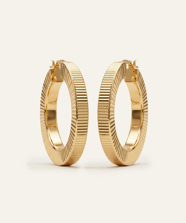 Gold hoop earrings with textured design on a light beige background