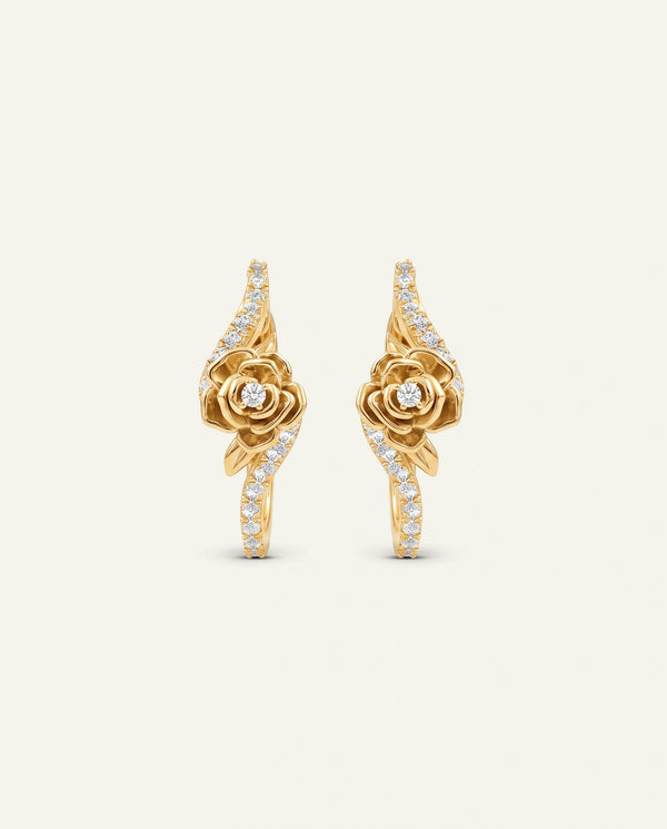 A pair of rose gold hoop-style drop earrings featuring a sculpted central rose motif with a small round diamond at the center, surrounded by curved ribbon-like bands studded with pavé diamonds, set against a plain off-white background.