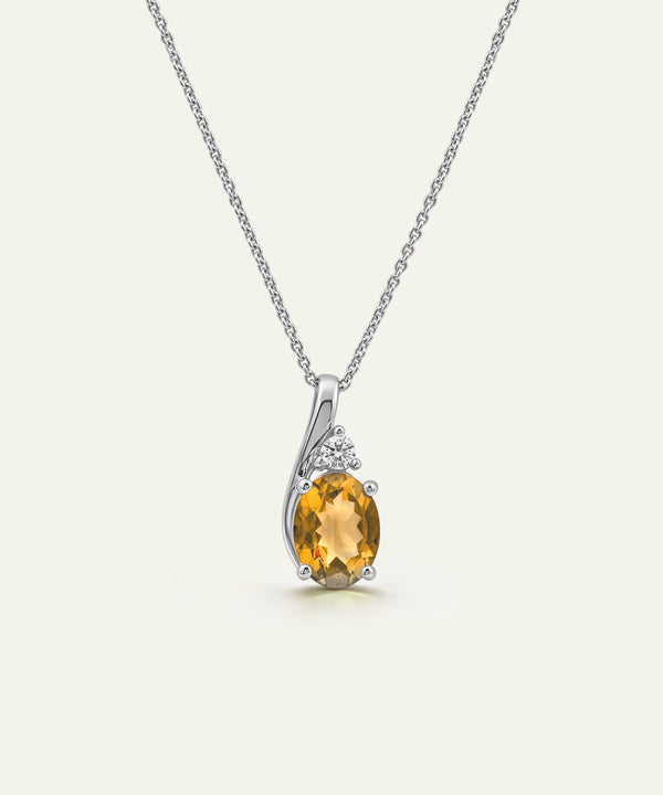 A silver pendant necklace featuring an oval-cut yellow citrine center stone and small clear accent stones, displayed on a clean off-white background.