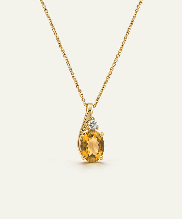 A yellow gold necklace with a curved pendant featuring a large oval-cut yellow citrine gemstone and a small clear accent stone, shown on a light cream background.