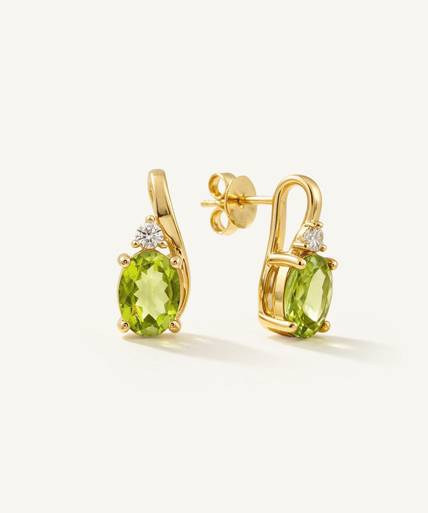 A pair of gold stud earrings featuring oval green peridot gemstones and small clear accent stones, shown on a clean off-white background.