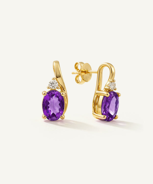 A pair of gold post earrings featuring oval purple amethyst gemstones and small clear accent stones, shown on a clean off-white background.