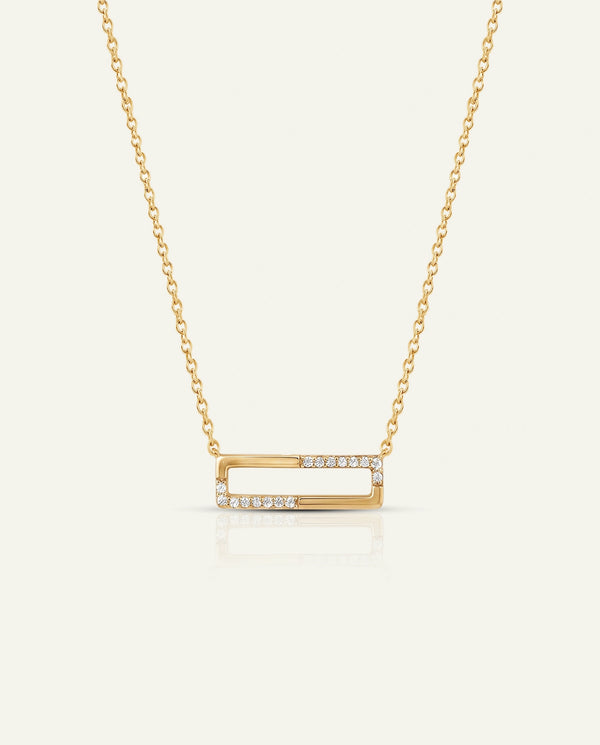 A gold open-bar necklace with a delicate chain and small clear stones set along the front edges of the bar, displayed on a light cream background.