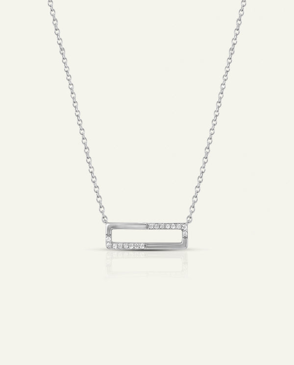 A silver-toned open rectangular bar necklace with a row of small clear stones on the right side, suspended from a delicate chain against a light cream background.