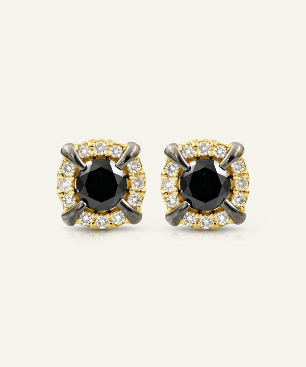 A pair of round stud earrings featuring a central black oval stone surrounded by a halo of small clear stones, with four curved dark metal prongs on each earring, shown on a light cream background.