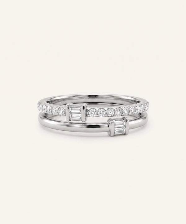 A pair of silver-toned stacking rings with baguette-cut diamonds, shown on a light cream background.