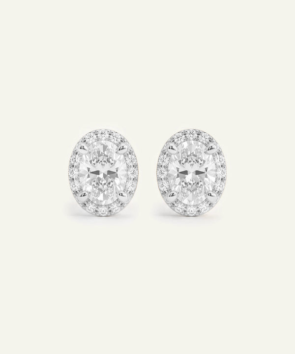 A pair of oval-cut diamond halo stud earrings in a silver setting.