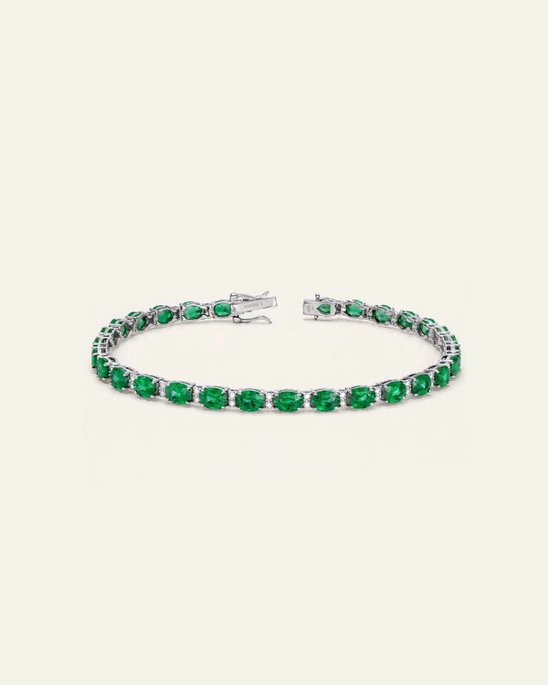 A tennis bracelet featuring round-cut green emeralds in a silver-toned setting, displayed on a light cream background.