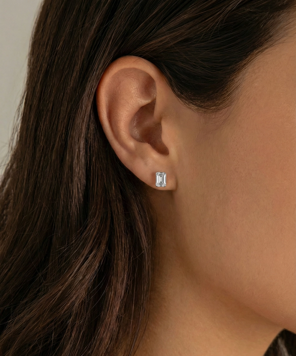 Close-up of an ear wearing a diamond stud earring with a neutral background