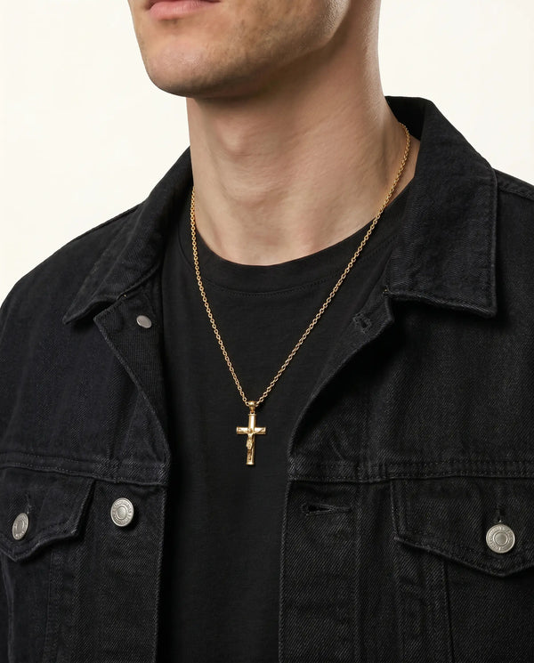 Person wearing a gold necklace with a cross pendant on a plain background