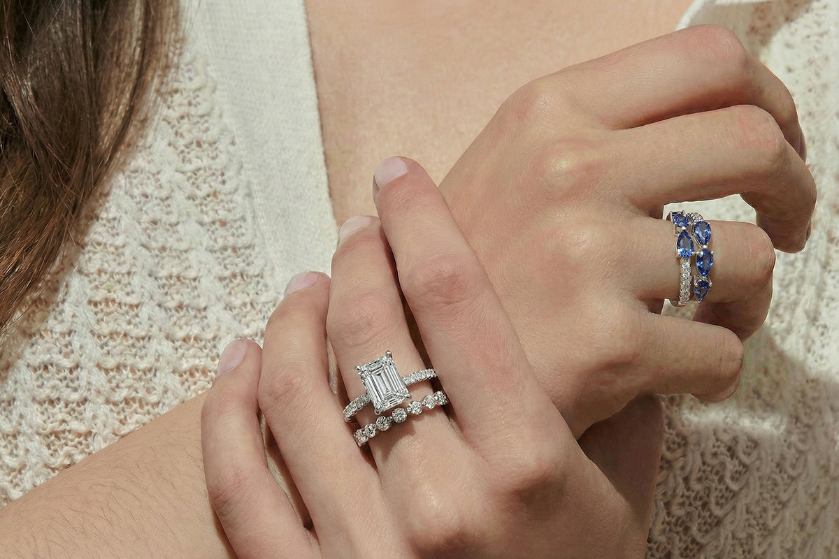 Close-up of two hands wearing diamond rings on a neutral background