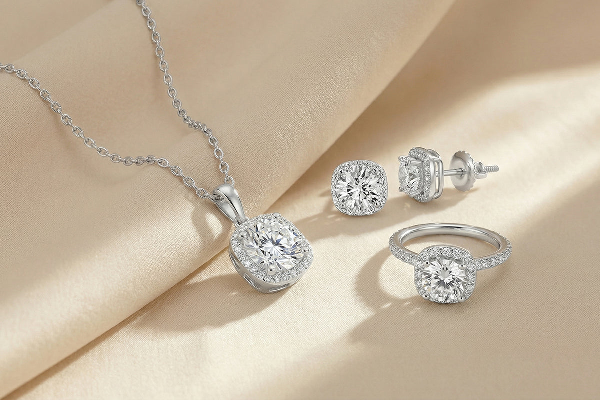 Elegant diamond jewelry set on a soft beige fabric, featuring a necklace, a pair of stud earrings, and a ring, each with square halo designs and sparkling round center stones.