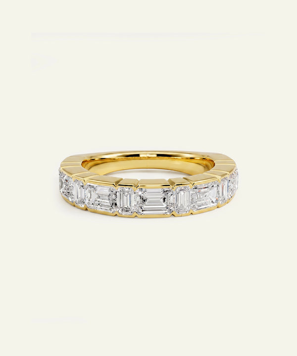 A yellow gold eternity ring featuring a row of baguette-cut clear diamonds, set against a plain off-white background.