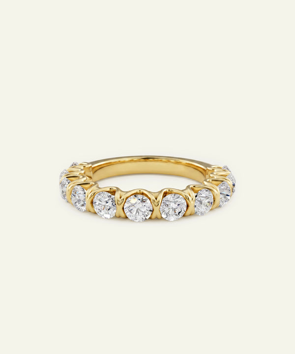 A yellow gold eternity ring featuring a row of round-cut clear gemstones in a prong setting, shown against a plain off-white background.
