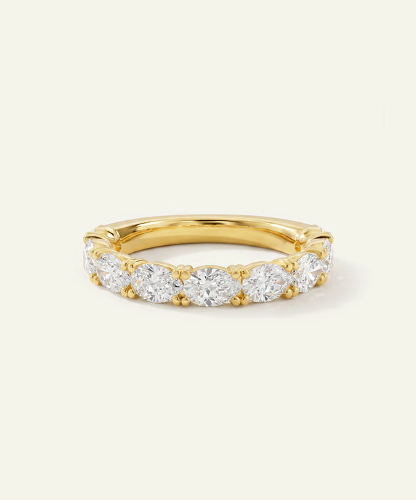 A yellow gold eternity ring featuring a row of round-cut clear gemstones, photographed on a clean, light off-white background.