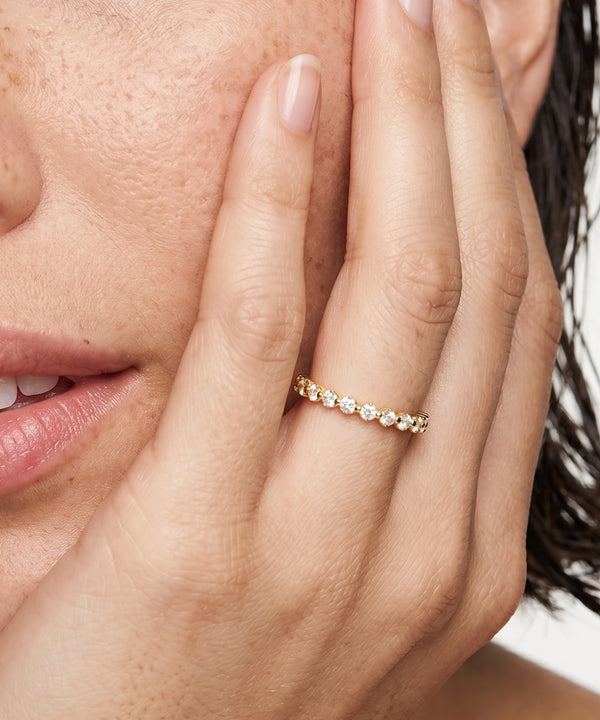 A close-up lifestyle shot of a woman wearing a silver eternity band ring set with small clear round-cut gemstones on her ring finger.