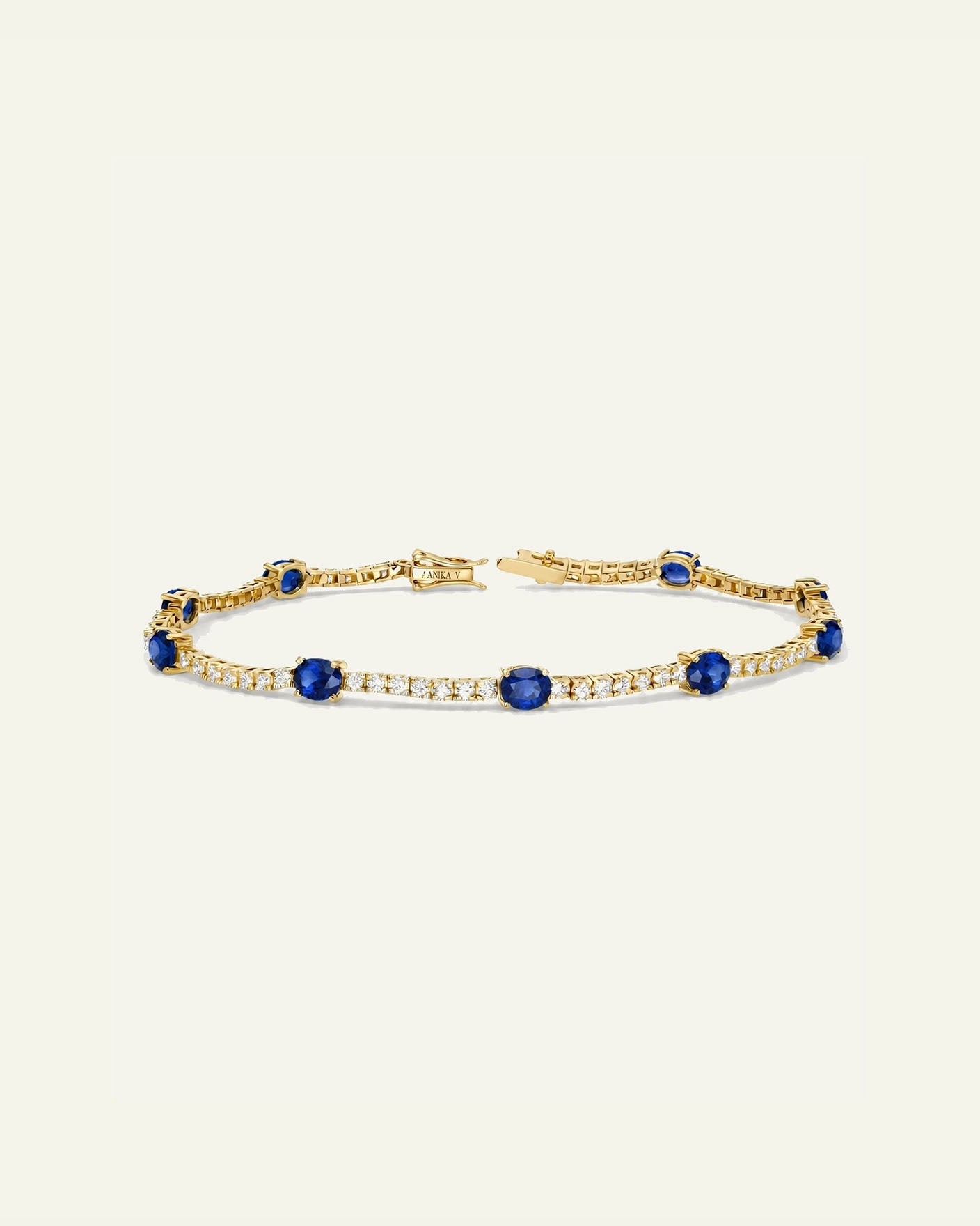 A yellow gold tennis bracelet featuring round-cut deep blue sapphires and rows of small clear stones, displayed on a solid off-white background.