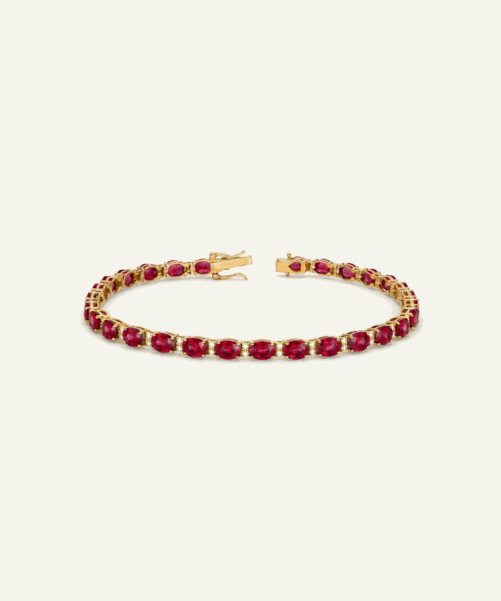 A gold tennis bracelet featuring a continuous row of oval-cut deep red gemstones, displayed on a clean, solid off-white background.