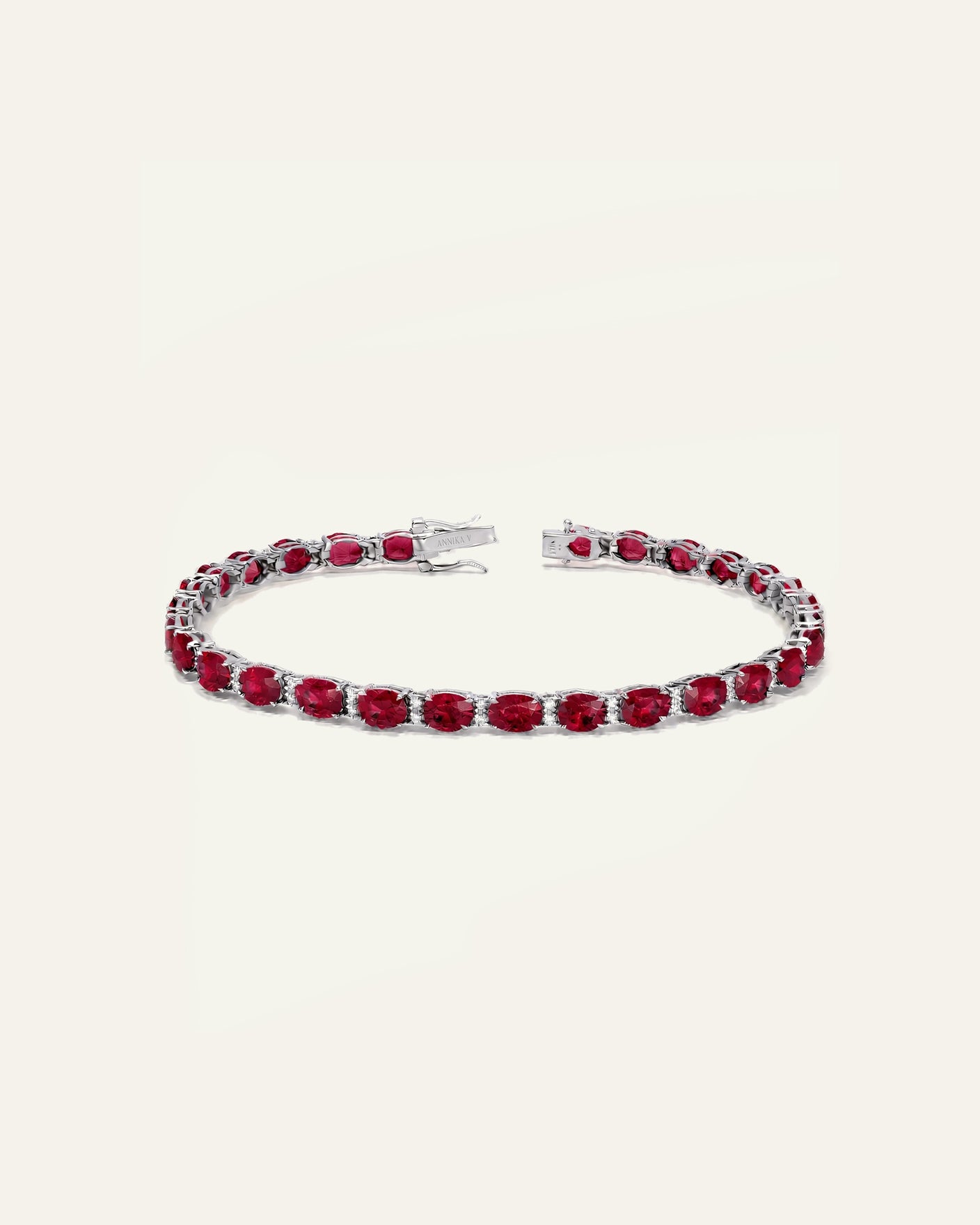 A silver-toned tennis bracelet featuring a continuous row of oval-cut deep red gemstones, displayed on a clean, solid off-white background.