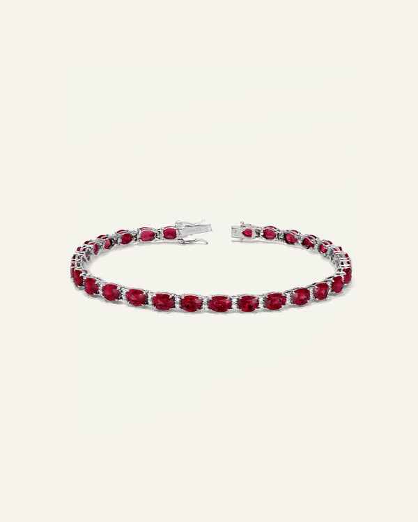 A silver-toned tennis bracelet featuring a continuous row of oval-cut deep red gemstones, displayed on a clean, solid off-white background.