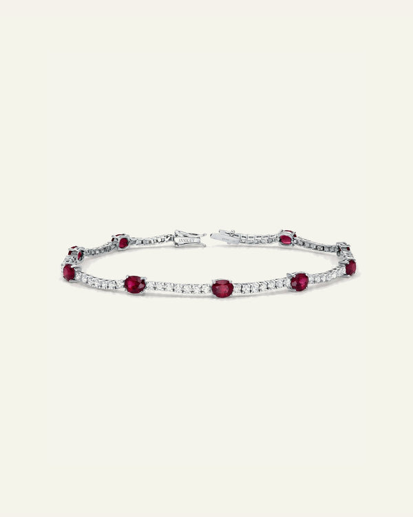 A silver tennis bracelet featuring oval red gemstones and rows of small clear stones, displayed on a light cream background.