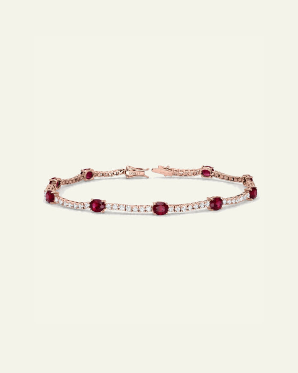 A rose gold tennis bracelet featuring round deep red rubies and rows of small clear stones, displayed on a light cream background.