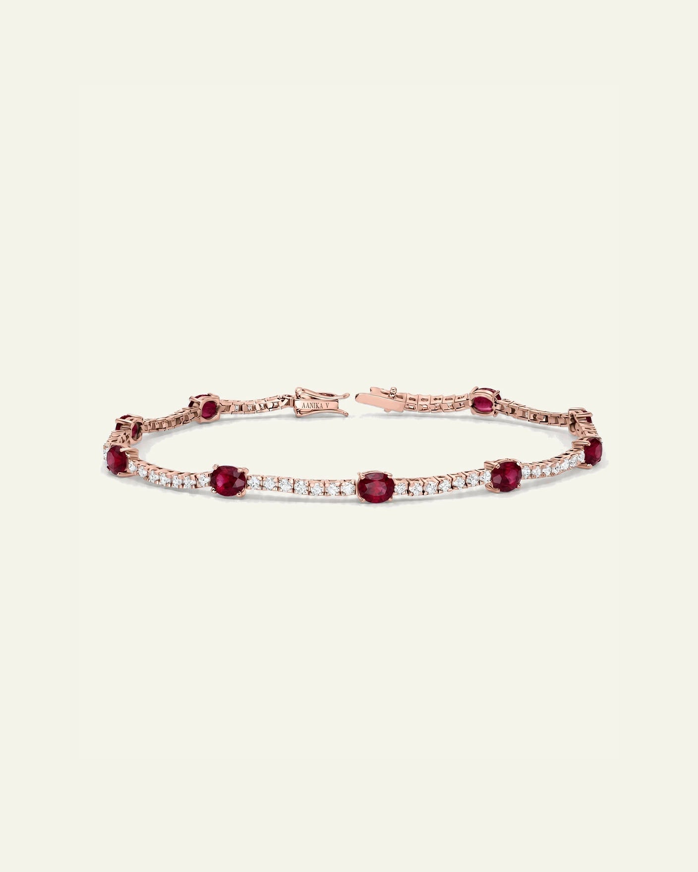 A rose gold tennis bracelet featuring round deep red rubies and rows of small clear stones, displayed on a light cream background.