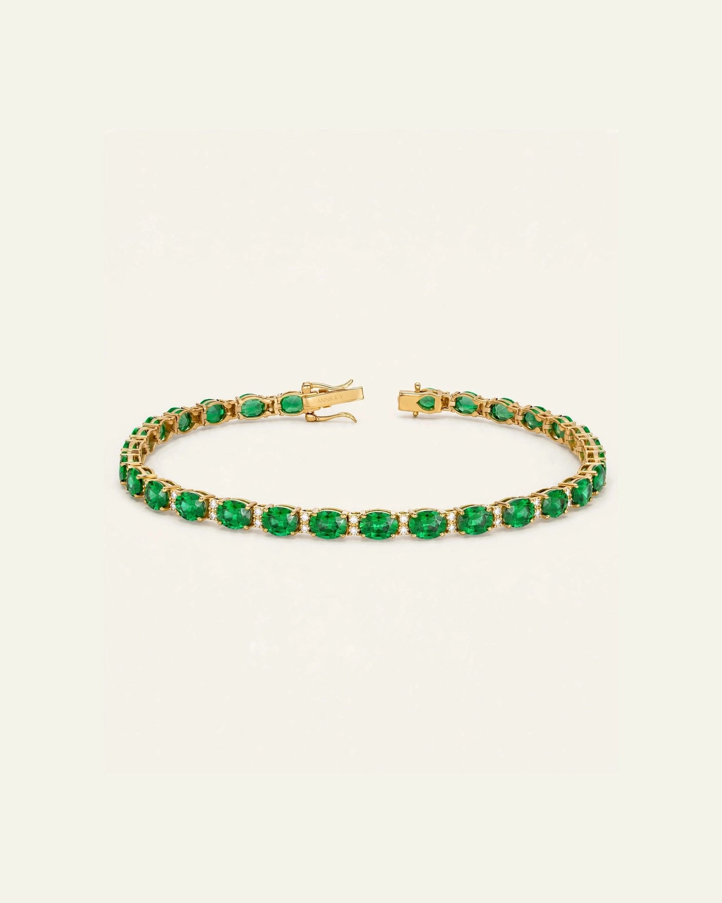 A gold tennis bracelet featuring a row of oval-cut green emerald-cut gemstones, displayed on a clean off-white background.