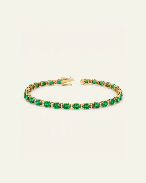 A gold tennis bracelet featuring a row of oval-cut green emerald-cut gemstones, displayed on a clean off-white background.
