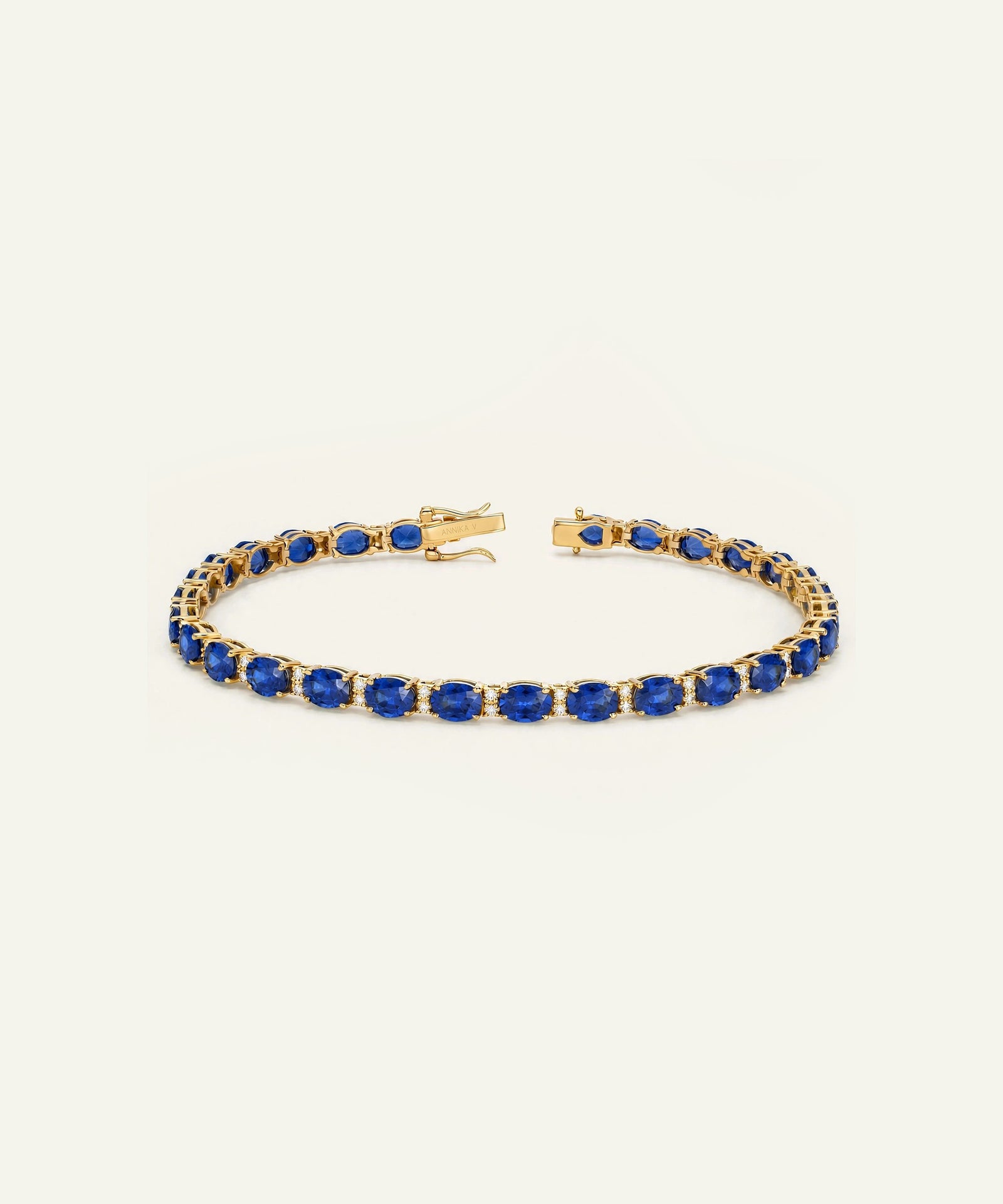 A gold tennis bracelet featuring a row of deep blue oval-cut gemstones, displayed on a clean, light off-white background.