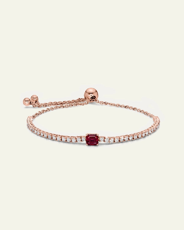 A delicate rose gold bracelet featuring a central cushion-cut red gemstone surrounded by small pavé-set clear stones, displayed on a light cream background.