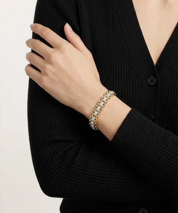 Person wearing a gold bracelet on a black ribbed sweater against a light background