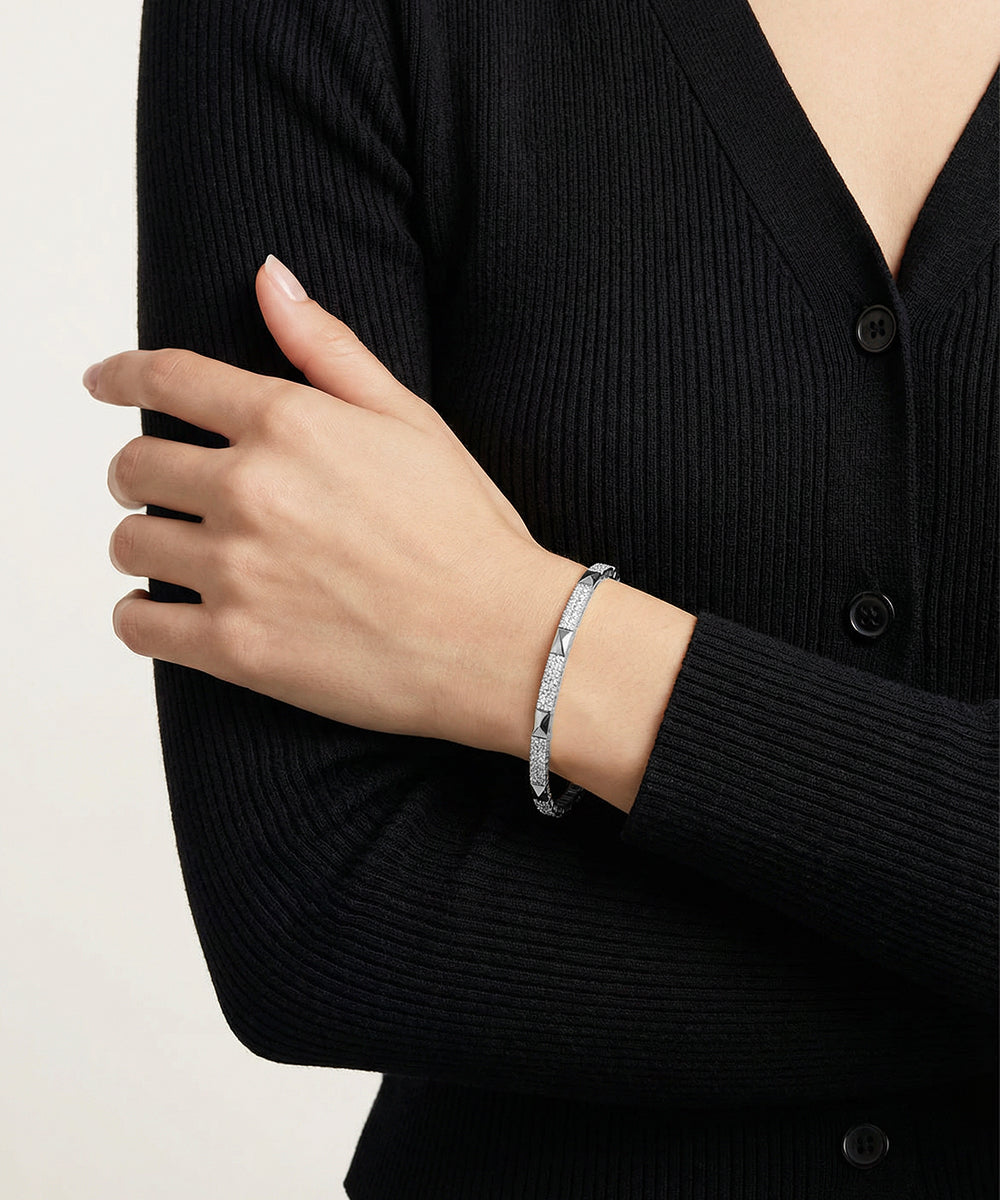 Person wearing a black cardigan with a silver bracelet on a plain background