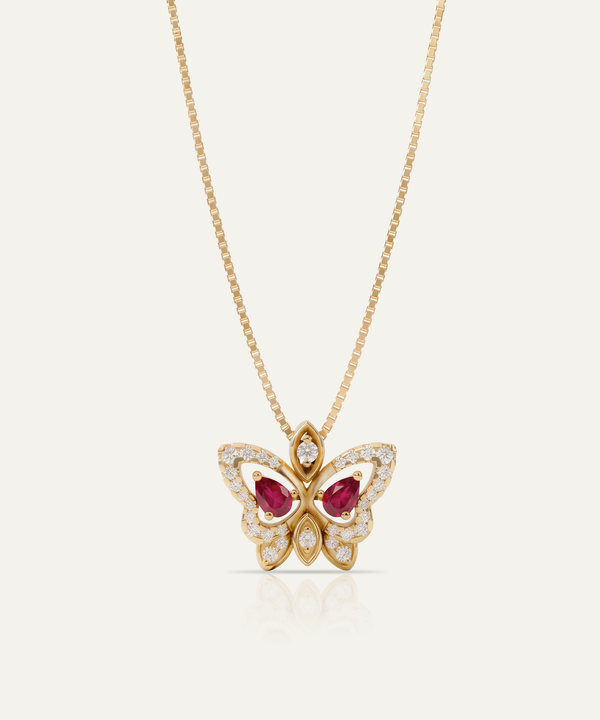 A gold butterfly pendant necklace featuring two marquise-cut red gemstones in the center and pavé-set clear stones along the wings, suspended from a delicate gold chain against a light cream background.