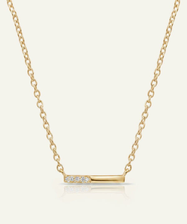 Gold necklace with a bar pendant on a light beige background