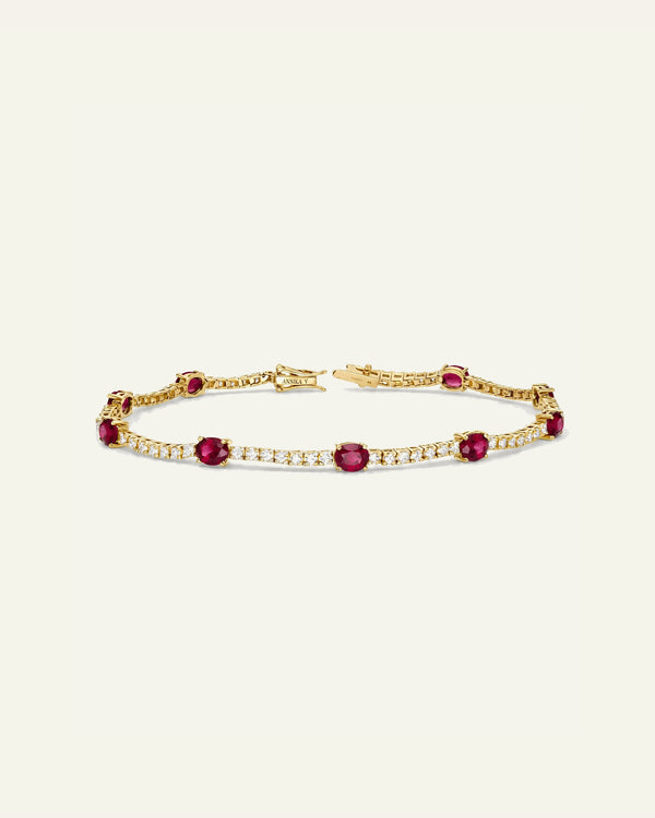A silver tennis bracelet featuring oval red gemstones and rows of small clear stones, displayed on a light cream background.