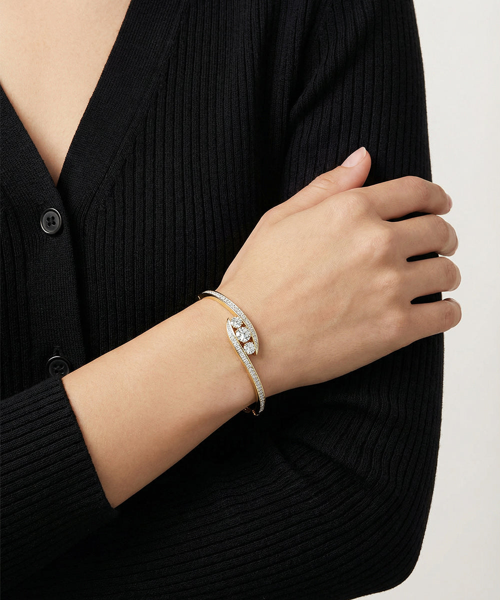Hand wearing a diamond bracelet with a black cardigan on a neutral background