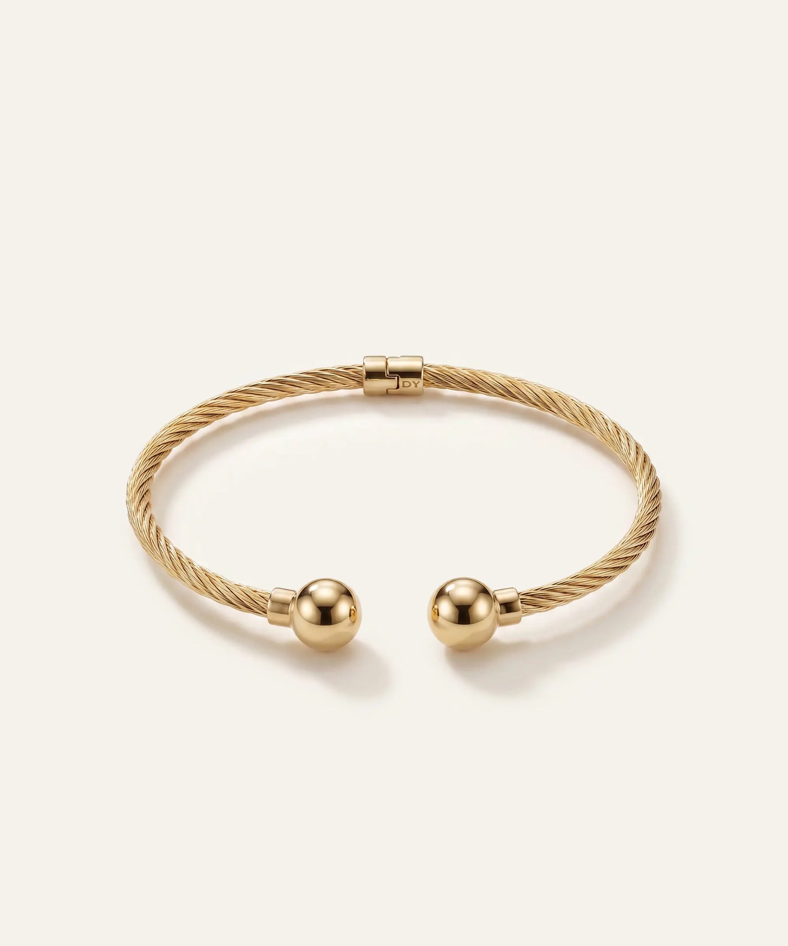 Gold bracelet with two spherical charms on a light beige background