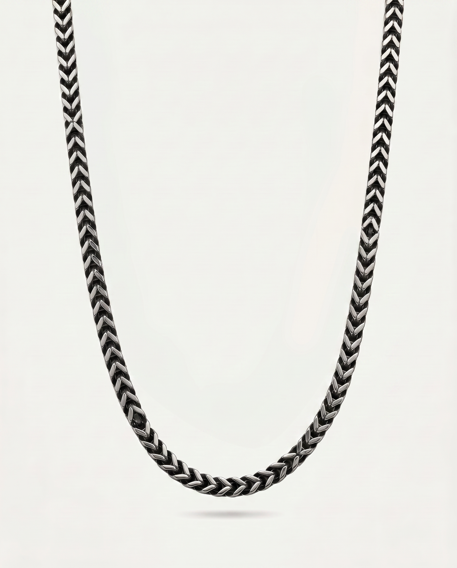 A close-up of a braided chain necklace in black and white, suspended against a plain light gray background.