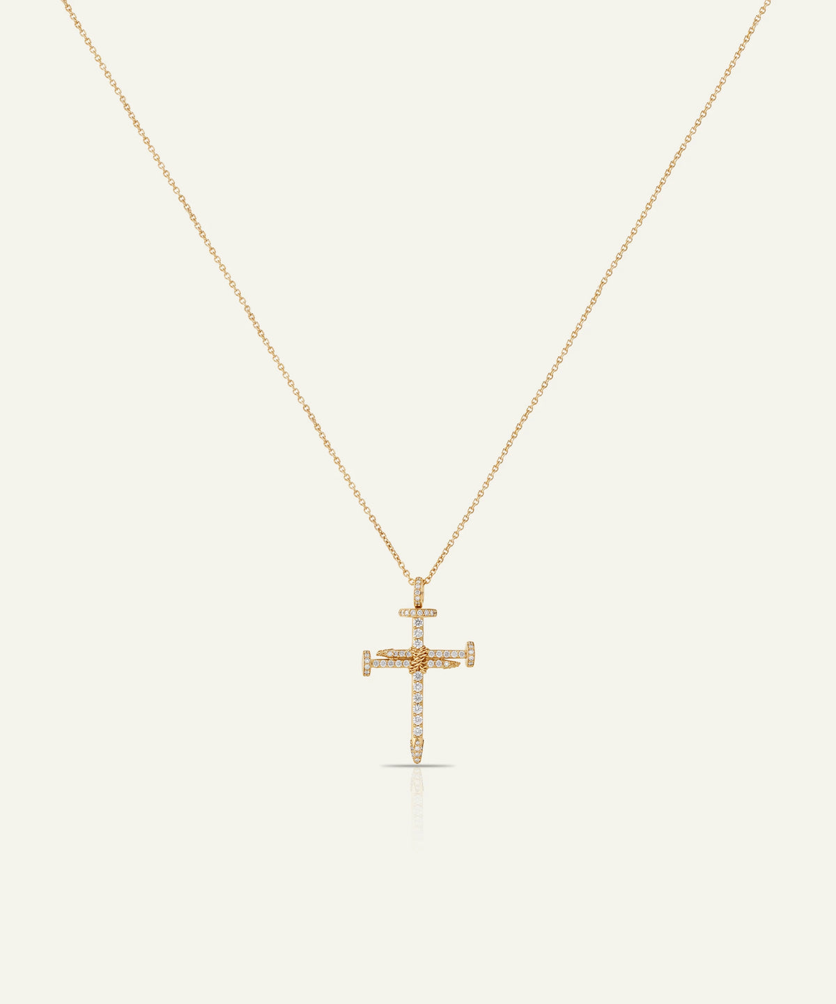 A delicate gold cross pendant necklace adorned with small clear stones, suspended from a fine gold chain against a light cream background.