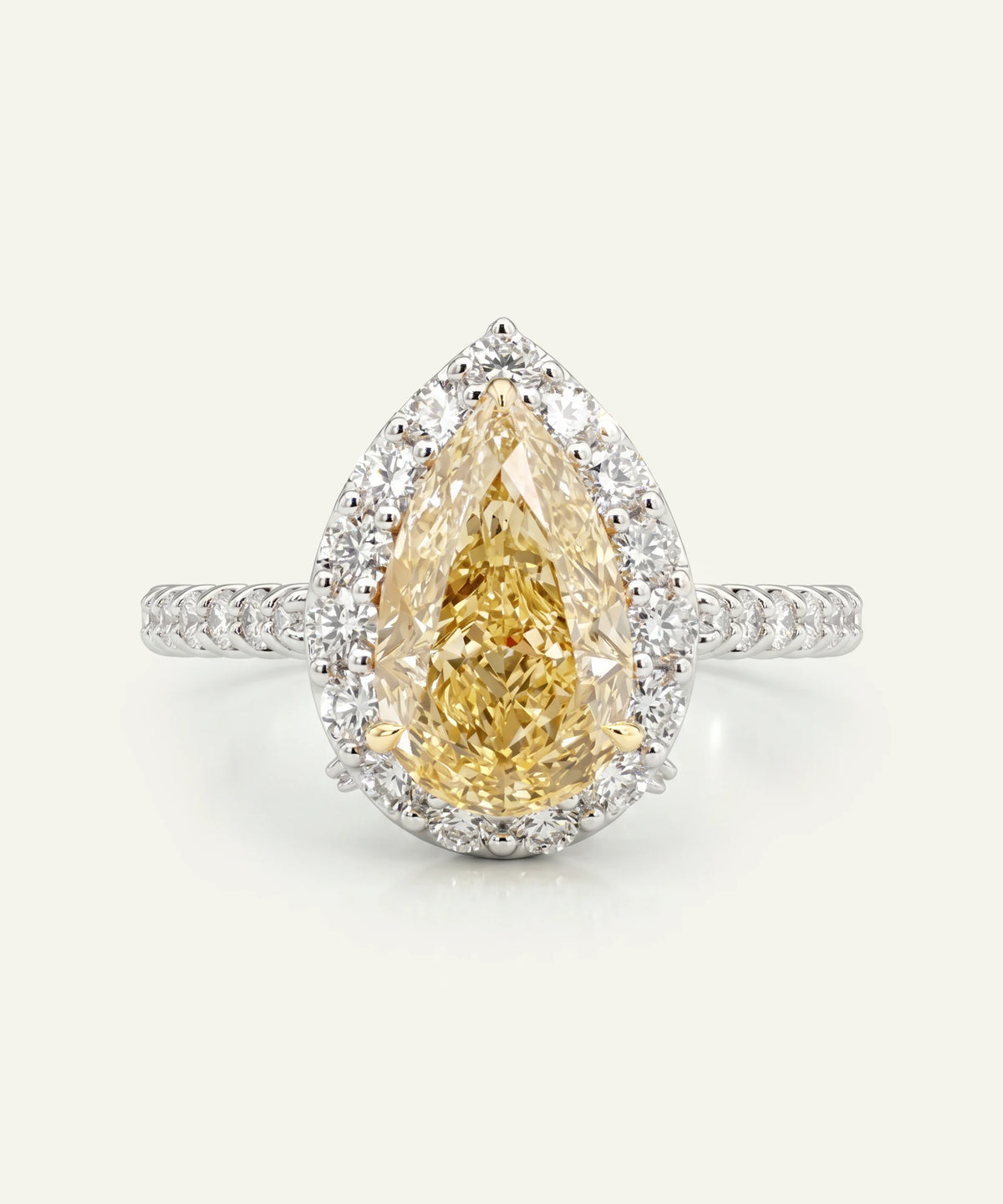 A platinum or white gold ring featuring a large pear-cut yellow diamond center stone with a halo of white diamonds and a pavé diamond band on a plain off-white background.