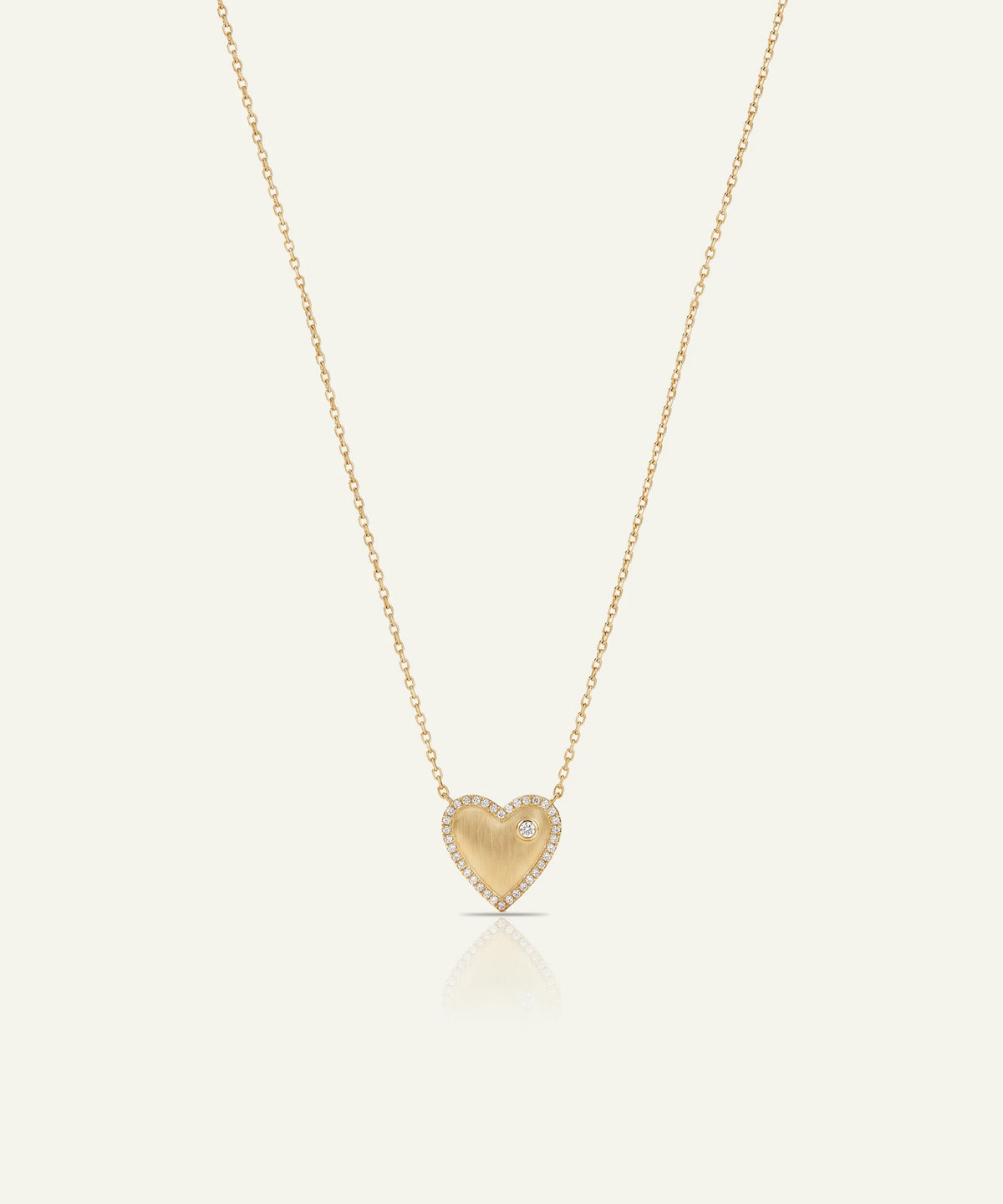 A delicate gold heart pendant necklace with a small clear gemstone, suspended from a fine gold chain against a light cream background.