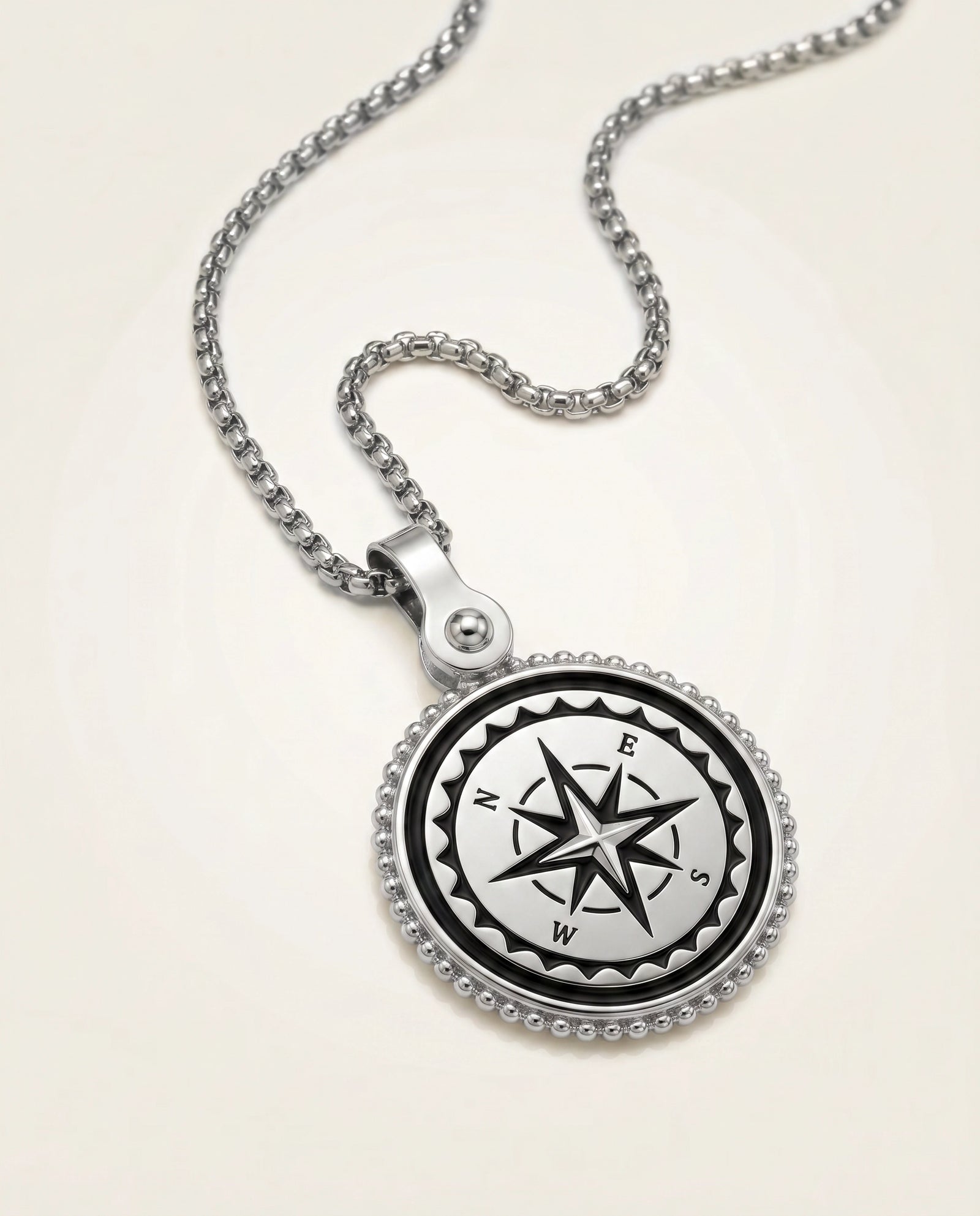 A silver compass pendant necklace on a matching silver box chain, displayed on a clean, light beige background.