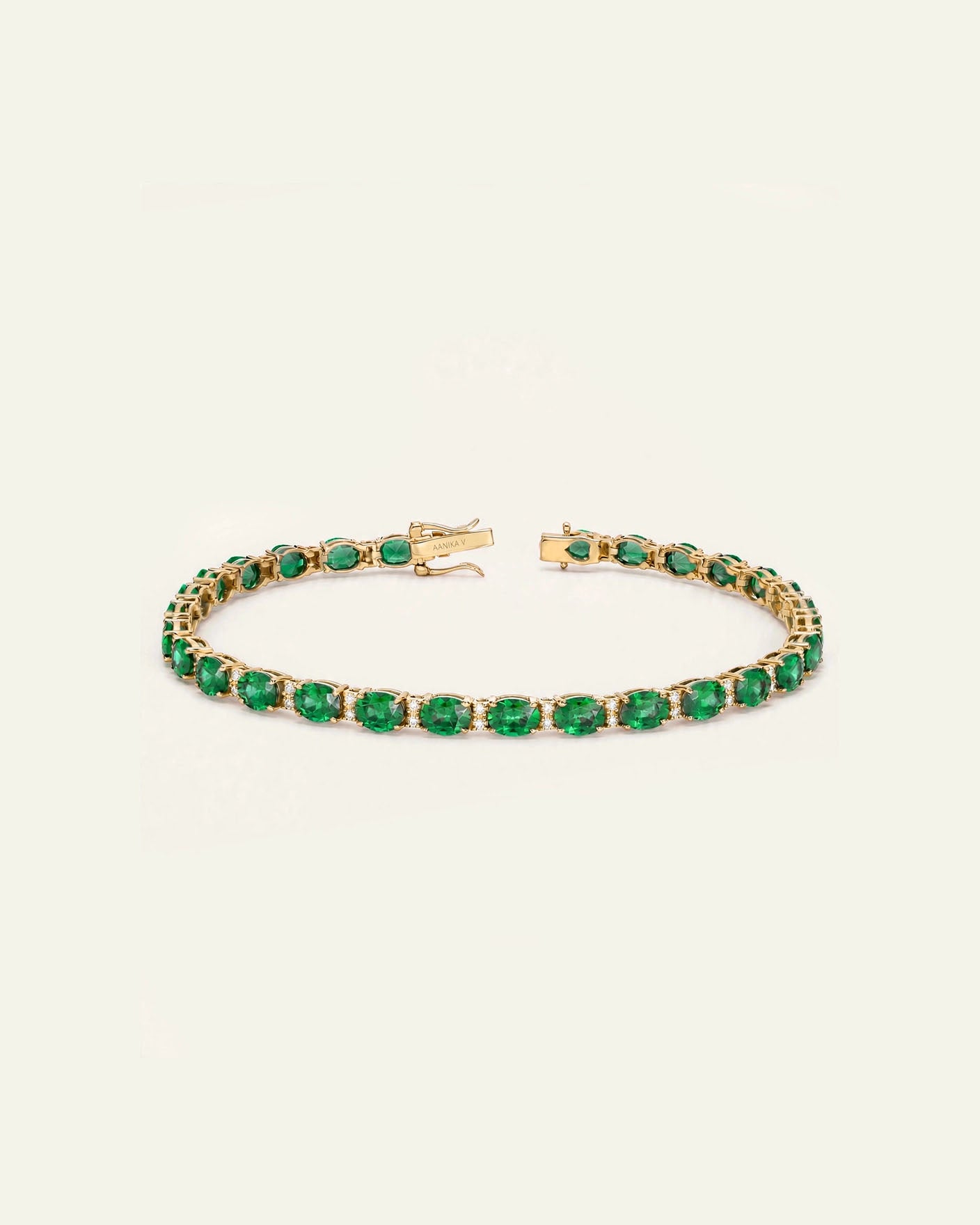 A gold tennis bracelet featuring a continuous row of round-cut green emeralds, displayed on a clean, off-white background.