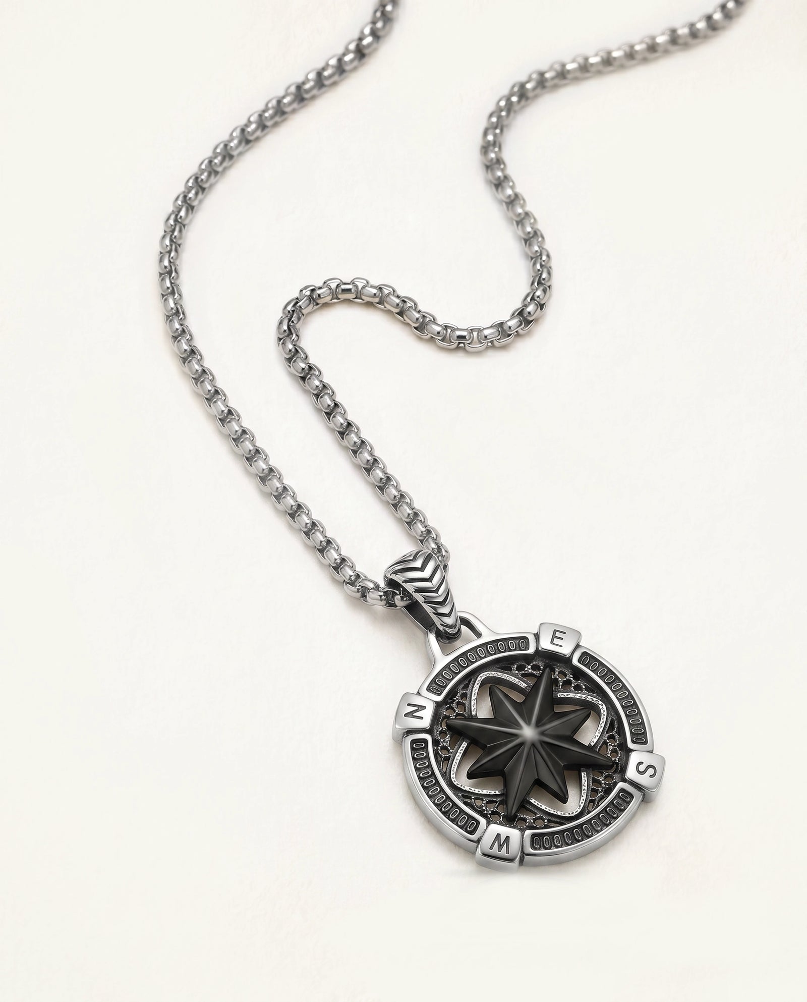 A silver-toned compass pendant necklace on a matching chain, displayed on a clean off-white background.