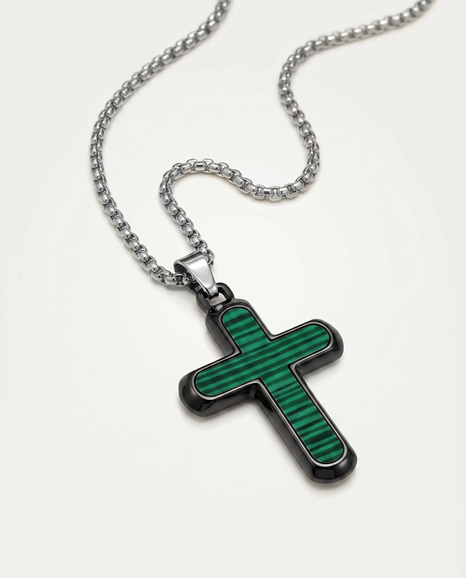 A silver-toned cross pendant necklace with a textured green inlay, displayed on a clean off-white background.