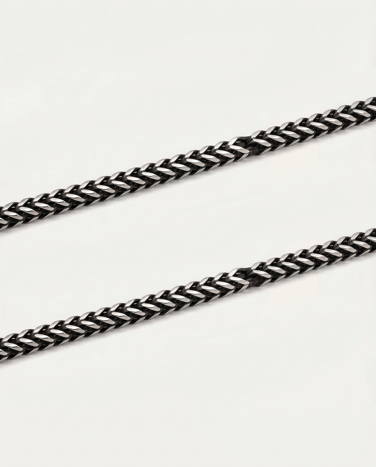 A close-up of a black and silver braided chain strap, likely for a watch or bracelet, laid diagonally on a plain off-white background.